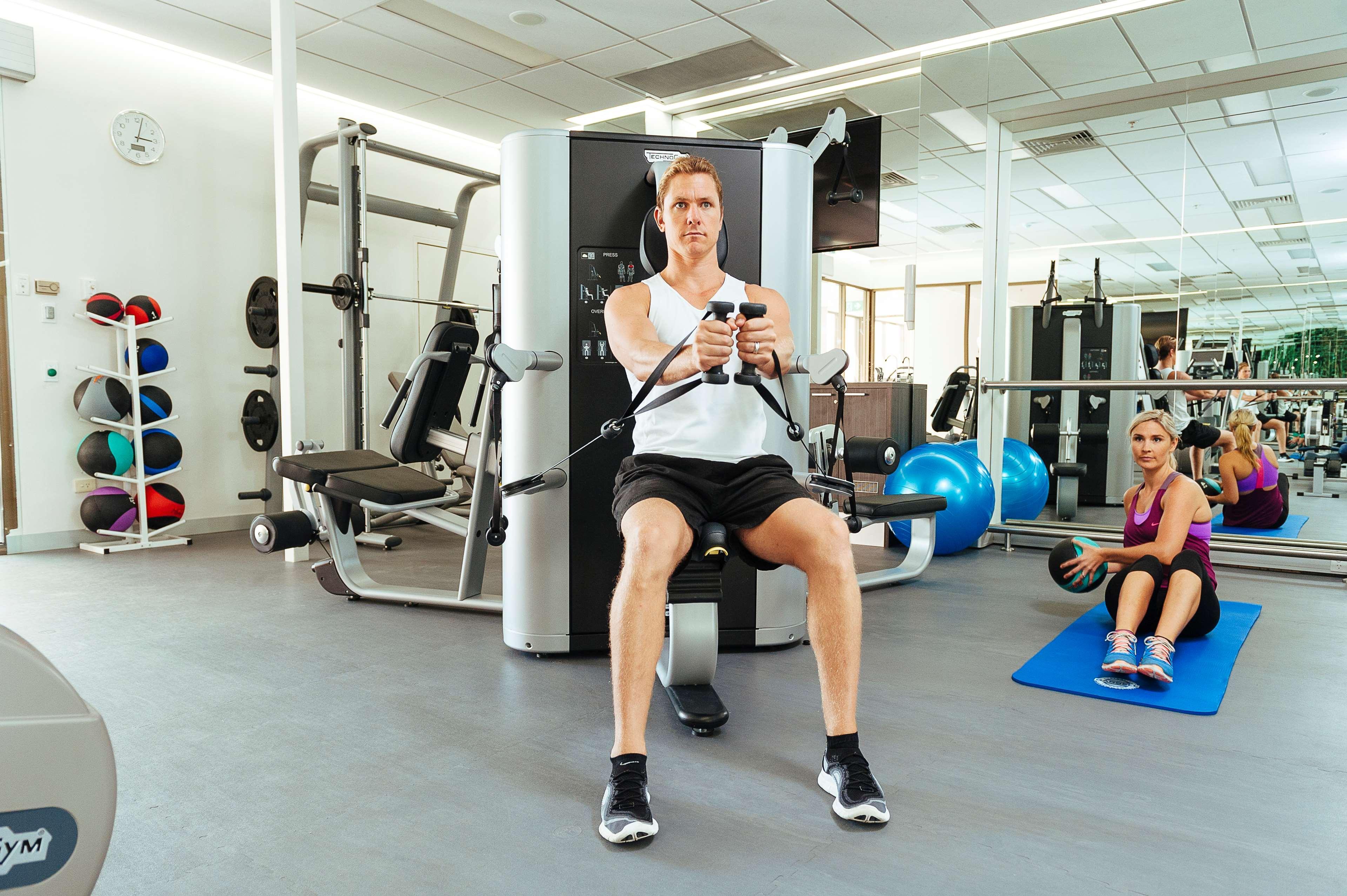 Stamford Plaza Adelaide Hotel Buitenkant foto The photo shows a gym setting with two individuals engaged in workout activities. 

In the foreground, a man is seated on a machine, using the handles to perform a rowing exercise. He is wearing a sleeveless shirt and shorts, indicating an active wor