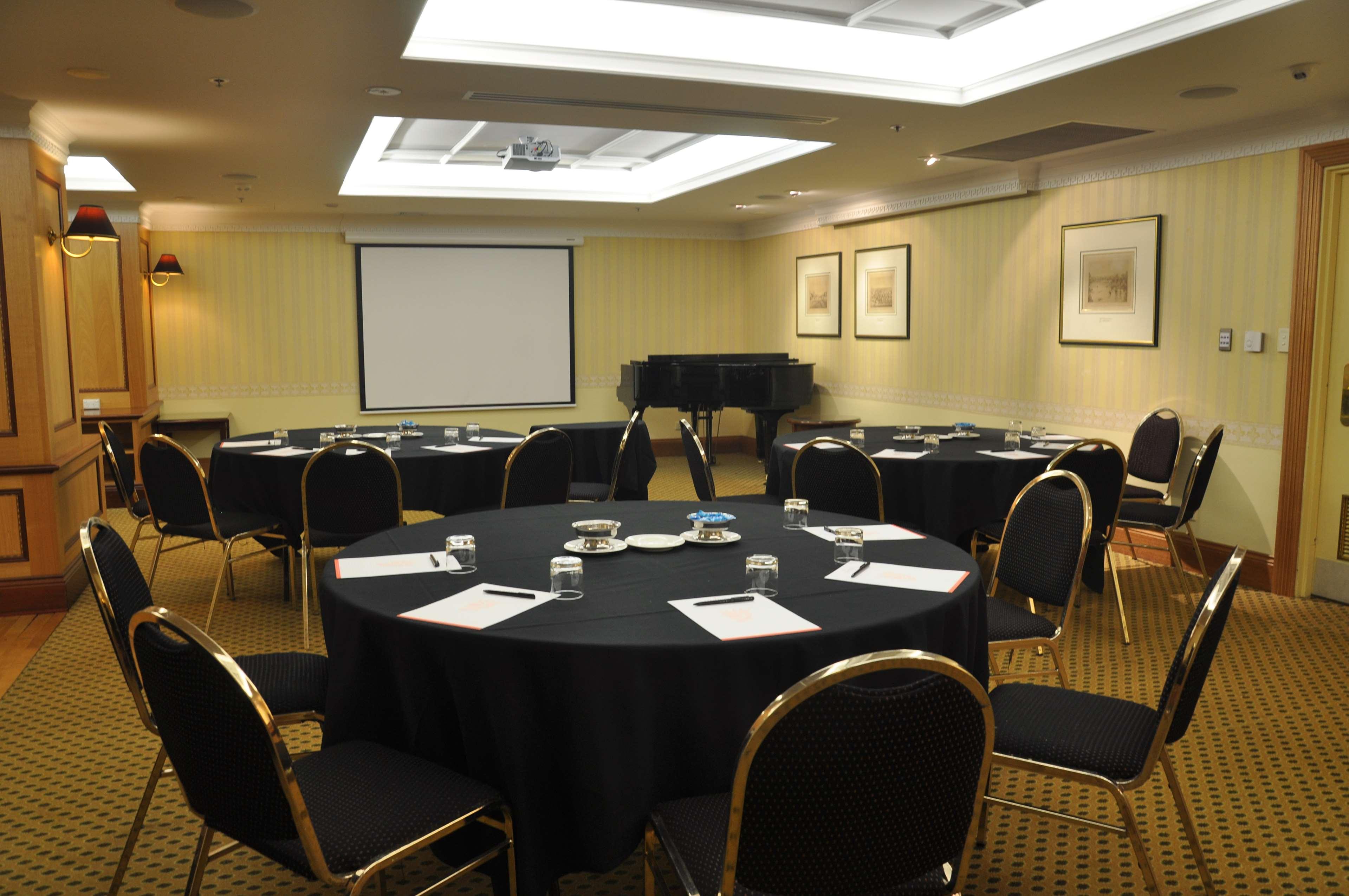Stamford Plaza Adelaide Hotel Buitenkant foto The photo shows a conference room set up for a meeting or presentation. There are several round tables covered with black tablecloths, each surrounded by black upholstered chairs. On the tables, there are notepads and glasses of water, indicating tha