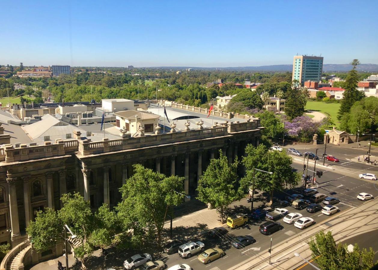 Stamford Plaza Adelaide Hotel Buitenkant foto The photo depicts a cityscape view, showcasing a mix of architectural structures and greenery. In the foreground, there is a large, classical building with columns, suggesting it may be a historical or governmental structure. Surrounding the building